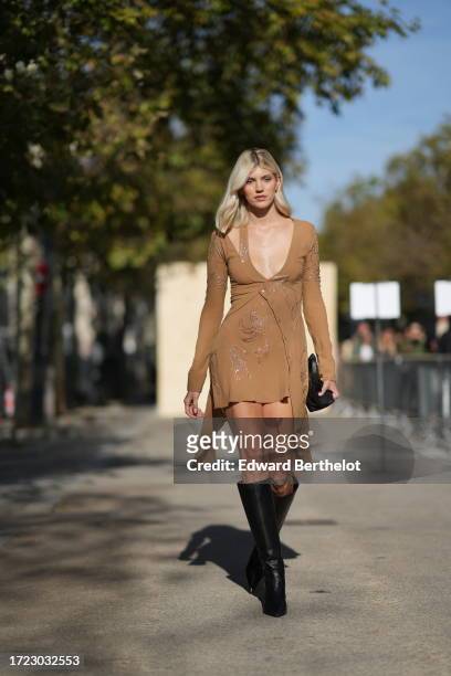 Devon Windsor wears, low neck brown dress with glitter / shiny details, knee high leather boot outside Stella McCartney, during the Womenswear...