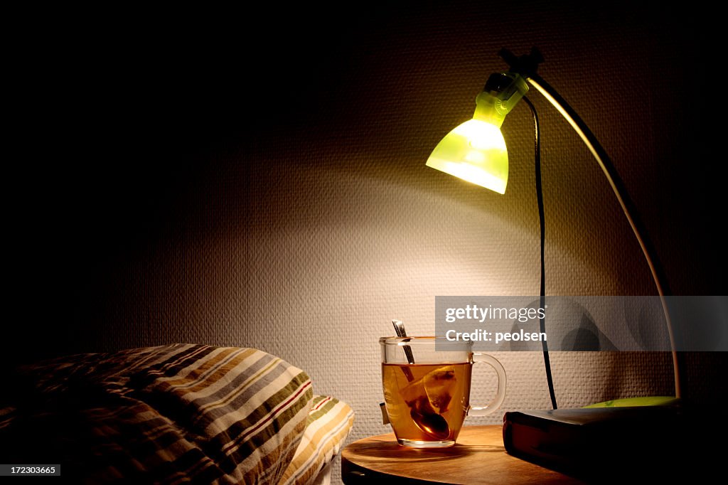 Bright bedside lamp with a clear cup of tea next to the bed