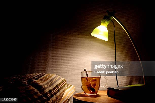 bright bedside lamp with a clear cup of tea next to the bed - te het dryck bildbanksfoton och bilder