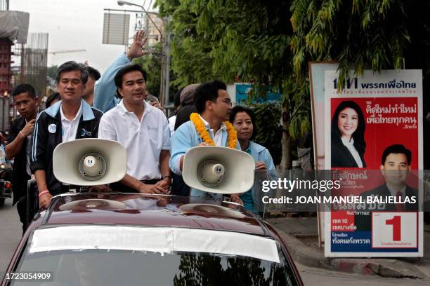 Ruling Democrat party candidate and incumbent Thai prime minister Abhisit Vejjajiva rides a pick-up truck past an electoral poster for his rival...