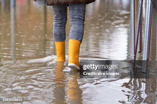 Rear view of a woman walking on the sidewalk of the street flooded by the rain with yellow boots Rear view of a woman walking on the sidewalk of the street flooded by the rain with yellow boots