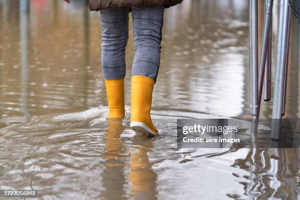 rear view of a woman walking on the sidewalk of the street flooded by the rain with yellow boots - yellow umbrella stock pictures, royalty-free photos & images