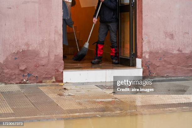 frontal view of two people sweeping the floodwater from the entrance of the house with brooms. - duct cleaning stock pictures, royalty-free photos & images