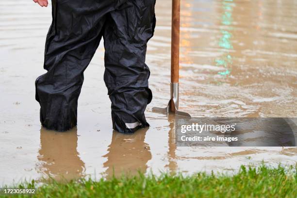 rear view of a person standing in the street flooded with water trying to unclog the sewer with a tool - inondation photos et images de collection