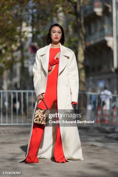 Guest wears a white trench coat, a red top with details and keyhole, flared pants, a brown leopard print bag, outside Stella McCartney, during the...