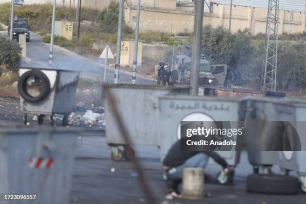 Palestinians take cover with trash containers as they clash with Israeli forces in Beit El district of Ramallah, West Bank on October 13, 2023.