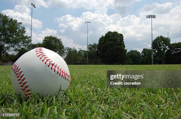 closeup of baseball sitting in grassy field under cloudy sky - baseball grass stock pictures, royalty-free photos & images