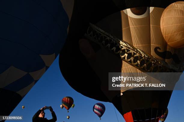 People take pictures as the Busby The King's Guard hot air balloon from the United Kingdom is inflated as it takes flight at sunrise during the...