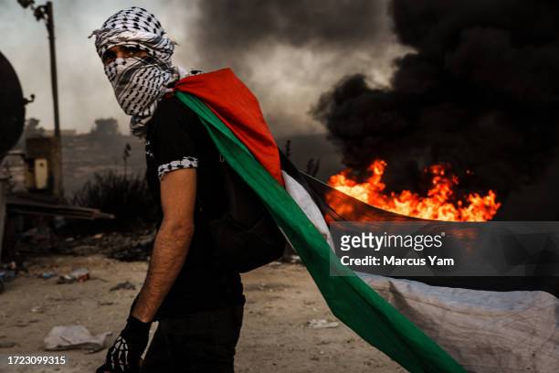 Palestinian dons a Palestinian flag during while protesting Israeli occupation in the West Bank, as protesters are met with tear gas, flashbang and...