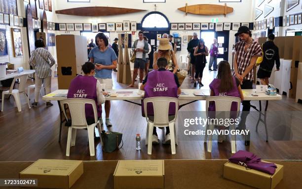 Voters collect their ballot papers from polling officers inside a polling station on Bondi Beach in Sydney on October 14 as polls open in Australia's...