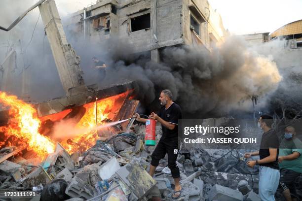 Graphic content / TOPSHOT - A Palestinian man uses a fire extinguisher to douse a fire following an Israeli strike, in Khan Yunis in the southern...