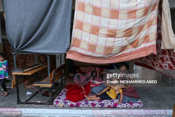 Graphic content / TOPSHOT - An internally displaced Palestinian man sits with a child on a mattress on the ground as they take refuge in a United...