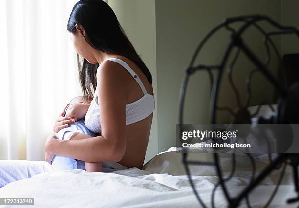 a mother nursing her baby on the edge of a bed - bra stockfoto's en -beelden