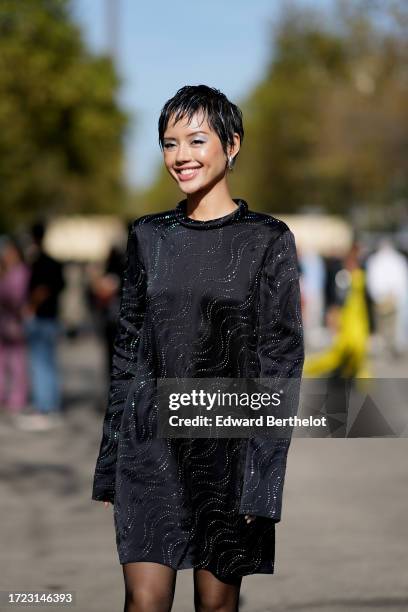 Khanh Linh wears earrings, a black lustrous silk mini dress with long sleeves and printed geometric patterns, outside Stella McCartney, during the...