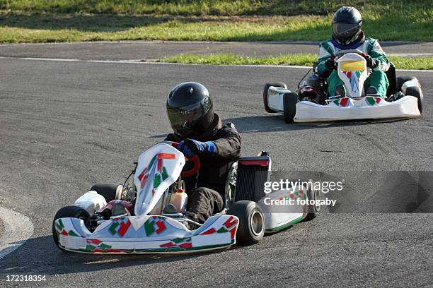 two people with helmets racing go-carts around a track - go karts stock pictures, royalty-free photos & images