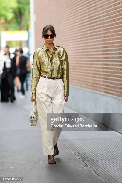 Guest wears sunglasses, a shiny bronze color shirt with pockets, a Fendi belt, cream color pleated pants, a multicolor Fendi bag, brown leather...