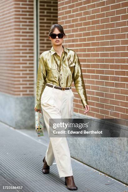 Guest wears sunglasses, a shiny bronze color shirt with pockets, a Fendi belt, cream color pleated pants, a multicolor Fendi bag, brown leather...