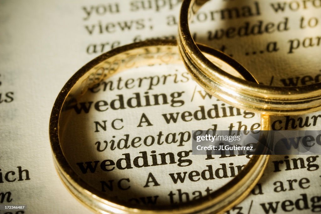 Two gold wedding bands on top of paper with the word wedding