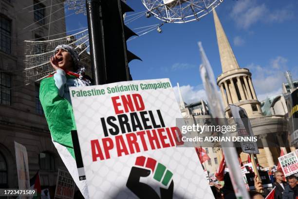 Protester climbs a set of traffic lights as people gather with placards to take part in a 'March For Palestine', part of a pro-Palestinian national...