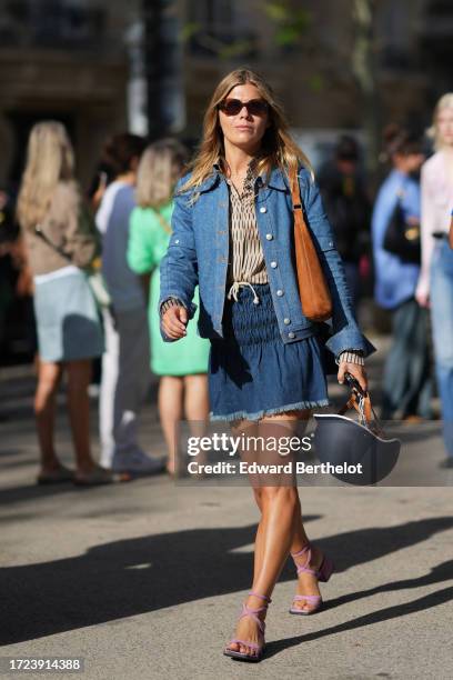 Guest wears sunglasses, a beige shirt with printed patterns, a blue denim jacket, a gathered blue ripped mini skirt, a helmet, purple lace up shoes,...