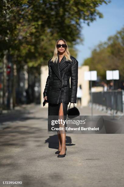 Candela Novembre wears sunglasses, a black leather quilted oversized blazer double breasted jacket, a slit skirt, a fluffy bag, pumps / shoes,...