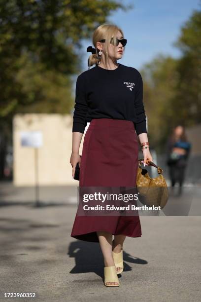 Guest wears sunglasses, a blac Prada pullover logo, a burgundy midi skirt, a brown woven leather bag, beige shoes, outside Stella McCartney, during...