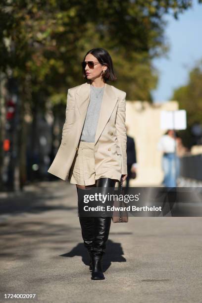 Erika Boldrin wears sunglasses, a gray top, a beige oversized blazer jacket, black leather thigh high boots, a beige leather bag, outside Stella...