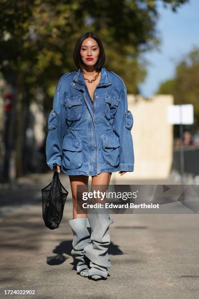 Tiffany Hsu wears a blue oversized denim jacket with several pockets, a black mesh bag, gray ruffled / gathered knee high oversized boots, outside...