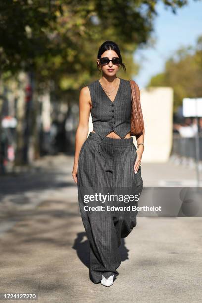 Bettina Looney wears sunglasses, a gray striped waistcoat, a brown leather bag, flared wide leg pants, outside Stella McCartney, during the...