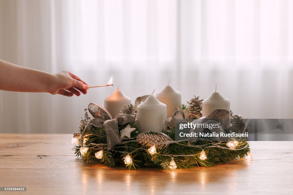 Child hand lighting the first candle on Advent Wreath to celebrate time before Christmas.