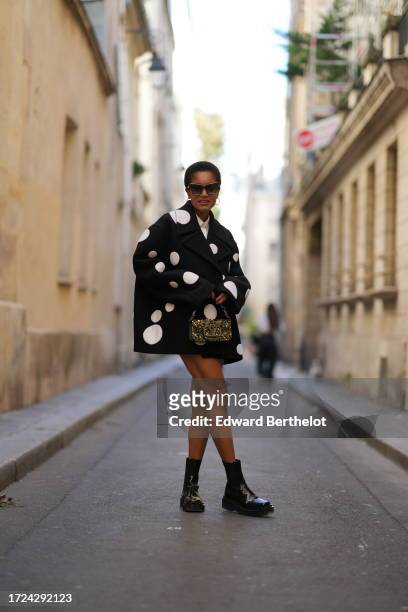 Tamu McPherson wears sunglasses, a white shirt, a black oversized blazer jacket with printed polka dots, a Valentino golden shiny glitter bag,...