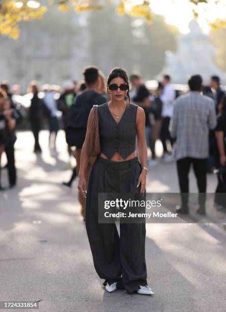 Bettina Looney is seen wearing a dark gray pinstripe vest, oversized pinstripe fabric pants, brown leather handbag by Miu Miu, gold earrings, gold...