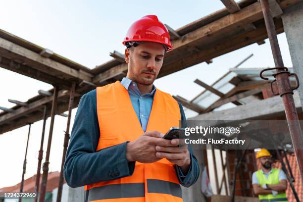 young caucasian engineer, using mobile phone, on a construction site - mobile developer stock pictures, royalty-free photos & images