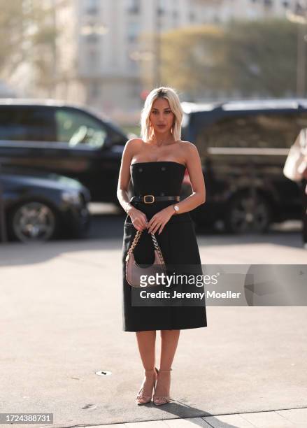 Model Roz is seen wearing an off shoulder black midi dress with black buttons, a black belt and gold buckle, beige high heels and a beige leather...