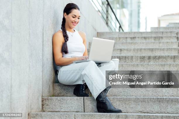 woman typing on a laptop while sitting on the stairs in the street - ärmelloses oberteil stock-fotos und bilder