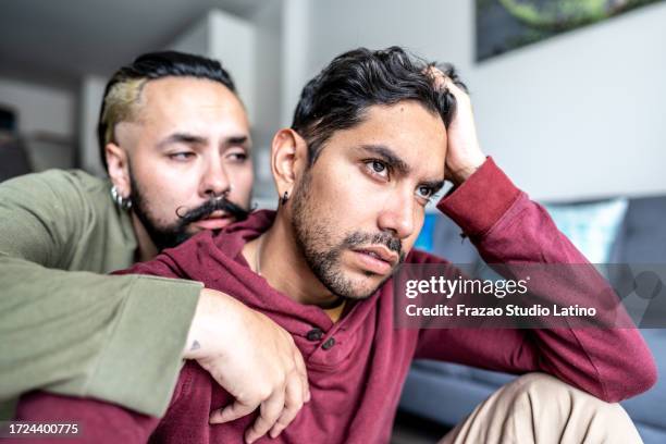 young man being comforted by his boyfriend at home - preconceito imagens e fotografias de stock