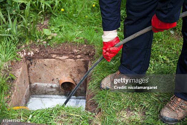 man with ground open unblocking a drain with a tool - riool stockfoto's en -beelden