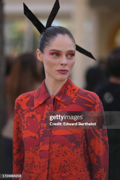 Coco Rocha wears a large hair bow tie, a red and orange floral print jacket, flared pants, outside Akris, during the Womenswear Spring/Summer 2024 as...