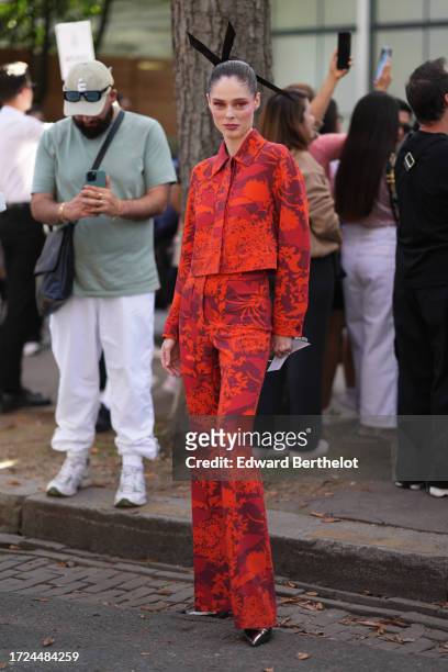 Coco Rocha wears a large hair bow tie, a red and orange floral print jacket, flared pants, outside Akris, during the Womenswear Spring/Summer 2024 as...
