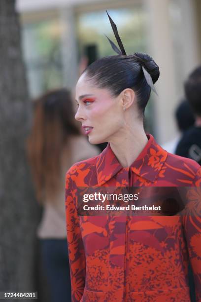 Coco Rocha wears a large hair bow tie, a red and orange floral print jacket, flared pants, outside Akris, during the Womenswear Spring/Summer 2024 as...