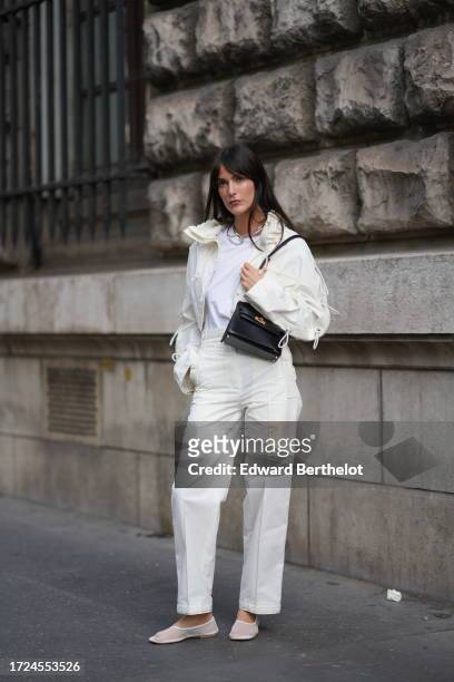 Guest wears a white jacket, a white t-shirt, white pants, a black leather Hermes bag, outside Hermes, during the Womenswear Spring/Summer 2024 as...