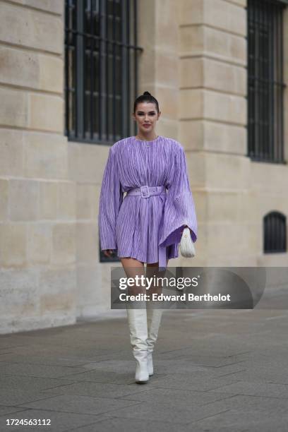 Polina Erofeeva wears a purple gathered short pleated dress, a belt, a Miu Miu bag, knee high white leather boots, outside Giambattista Valli, during...