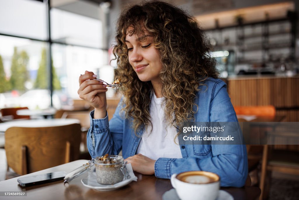 Giovane donna felice che mangia budino di chia per colazione al bar