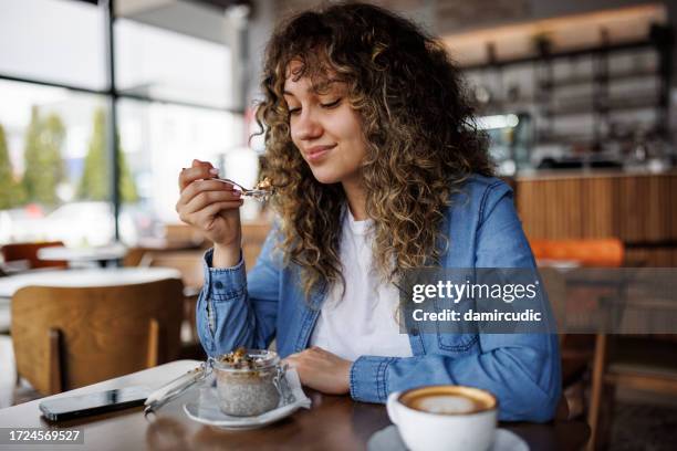 young happy woman eating chia pudding for breakfast at cafe - mousse stockfoto's en -beelden