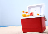 Red cooler full of fruit and juice on the beach