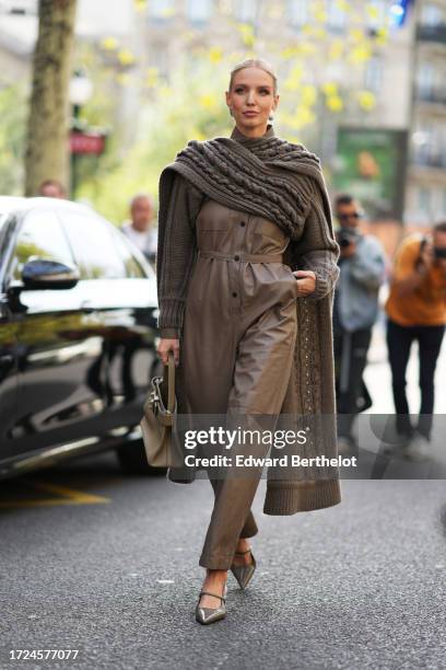 Leonie Hanne wears a khaki oversized knit long pullover worn as a cape, a brown leather jumpsuit, a Hermes bag, outside Hermes, during the Womenswear...