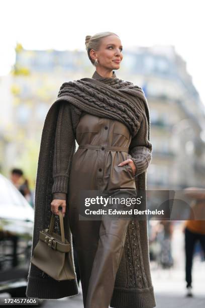 Leonie Hanne wears a khaki oversized knit long pullover worn as a cape, a brown leather jumpsuit, a Hermes bag, outside Hermes, during the Womenswear...