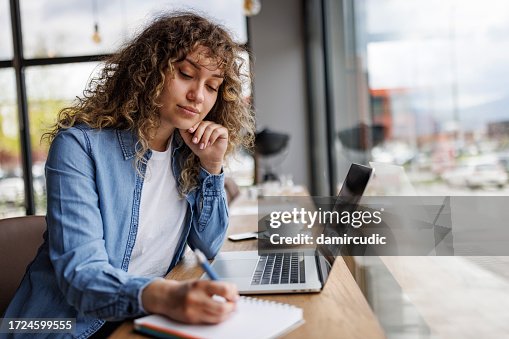 Junge Frau arbeitet am Laptop und macht sich Notizen in einem Café Junge Frau arbeitet am Laptop und macht sich Notizen in einem Café