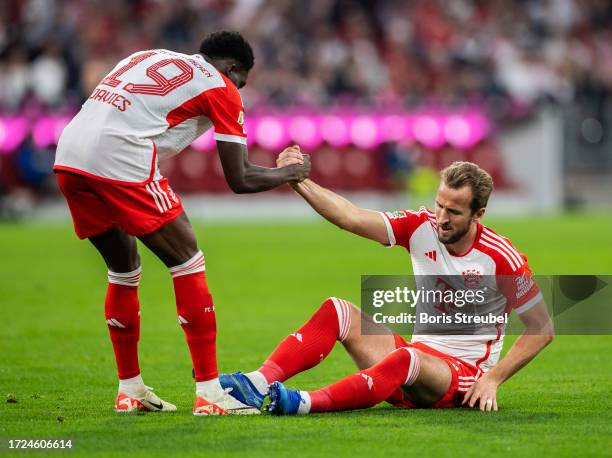 Alphonso Davies of FC Bayern Muenchen helps Harry Kane of FC Bayern Muenchen back on his feetduring the Bundesliga match between FC Bayern München...