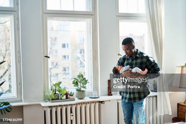 young father holding sleeping newborn baby in living room - lullaby stock pictures, royalty-free photos & images